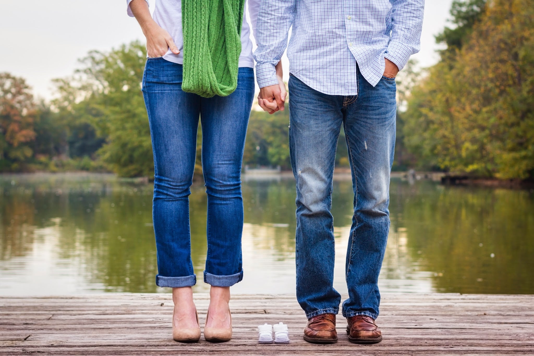 A Millennial couple holds hands while standing next to a pair of baby shoes